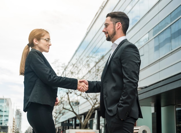 Businessman and businesswoman standing outside the office building shaking each others hand