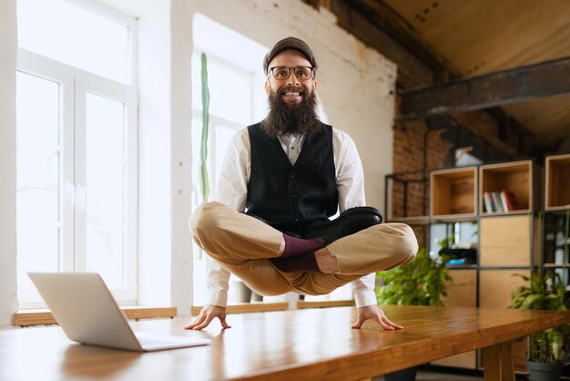 仕事の後に瞑想する作業テーブルでオフィスでヨガのポーズで立っているビジネスマンの陽気な従業員
