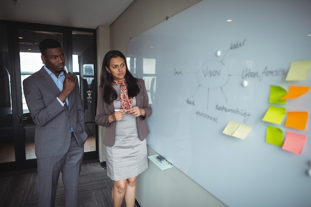 Businessman and a colleague looking at white board in conference room