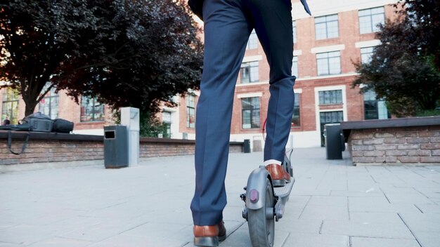 Businessman in diplomatic suit riding on electric scooter going to startup company office meeting enjoying using e-scooter vehicle in city street. Concept of eco-friendly transportation