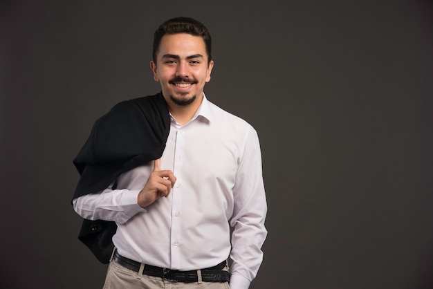 A businessman in dress code holding a black jacket in his shoulder. 