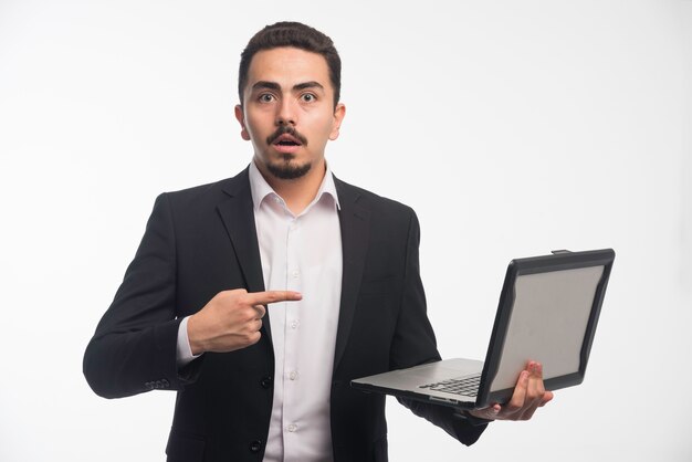 A businessman in dress code holding a laptop and pointing at it.