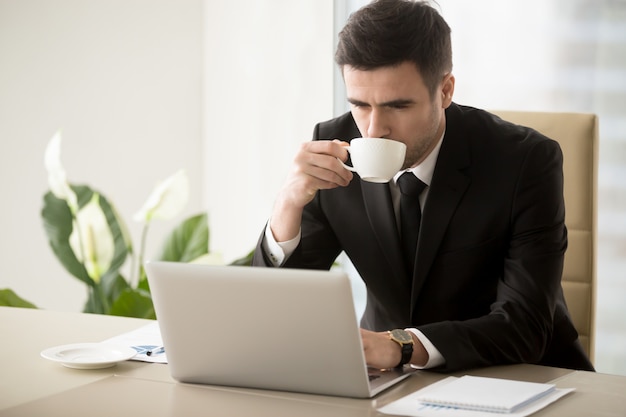 ビジネスマンのオフィスで働くときにコーヒーを飲む