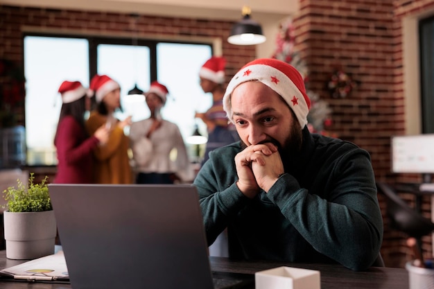 Businessman feeling disturbed at office job because of noisy coworkers celebrating christmas eve. Tired irritated employee being overwhelmed and working during winter holiday season.