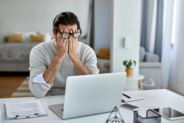 Businessman feeling exhausted after working on laptop at home