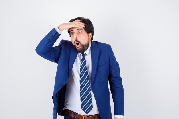 Businessman in formal suit holding hands on forehead and looking surprised , front view.