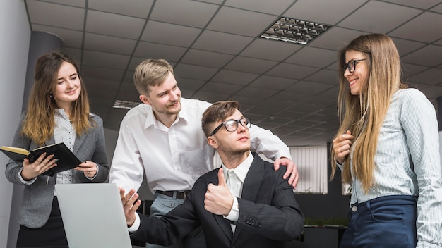 Free photo businessman gesturing thumbs up to his partners at workplace