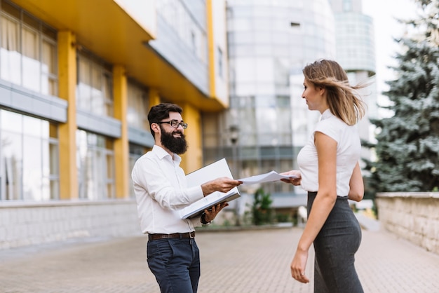 Businessman giving document to her female employee standing outside the office building