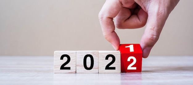Рука бизнесмена держа деревянный куб с перевернутым текстом блока 2021-2022 на фоне таблицы. решение, стратегия, решение, цель, бизнес и концепции новогодних праздников