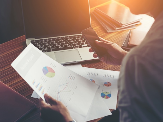 Businessman hands using cell phone with financial report graph a