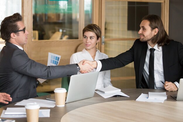 Businessman handshaking new colleague during team meeting