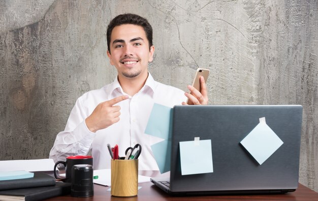 Businessman happily pointing his telephone at the office desk.