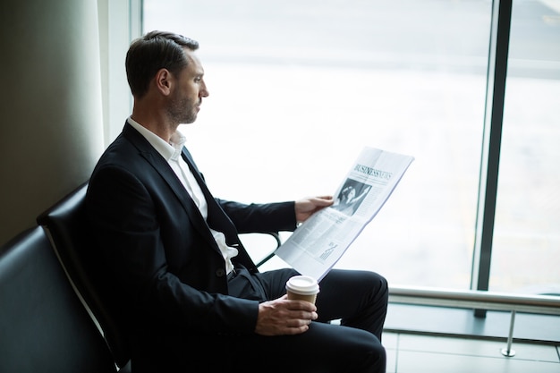 待合室で新聞を読みながらコーヒーを飲むビジネスマン