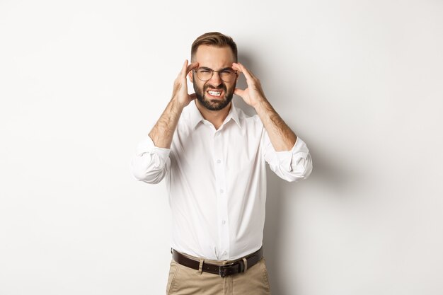 Businessman having headache, grimacing and holding hands on head, standing  