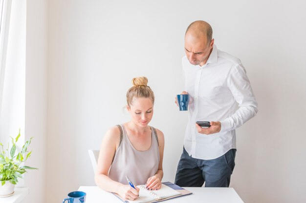 日記で書く女性を見ている電卓とコーヒーカップを持つビジネスマン