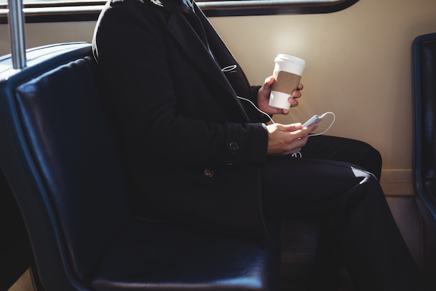 Foto gratuita uomo d'affari che tiene una tazza di caffè eliminabile e che per mezzo del telefono cellulare