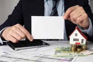 Free photo businessman holding an empty card next to a miniature house