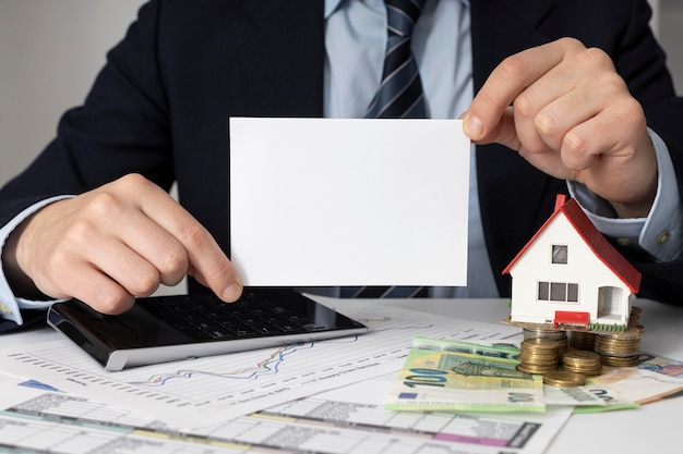 Businessman holding an empty card next to a miniature house