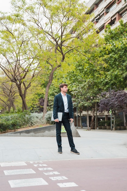 Businessman holding laptop in his hand standing in front of building