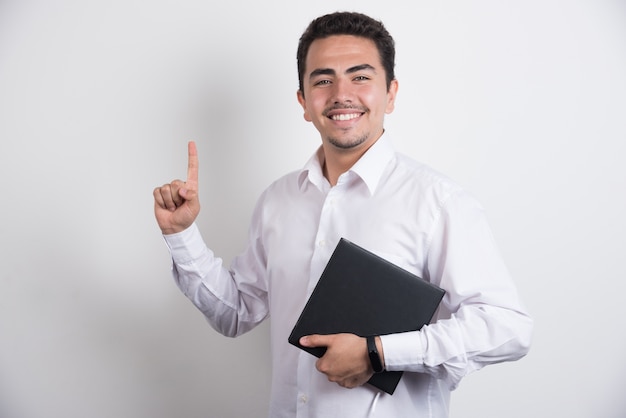 Businessman holding laptop and pointing up on white background.