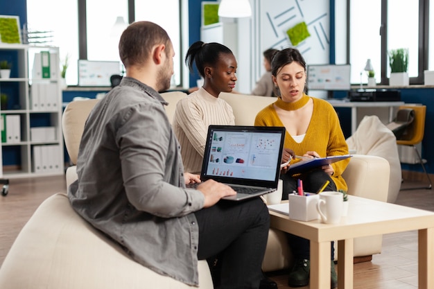 Businessman holding laptop with financial ghraphics while diverse employees talking