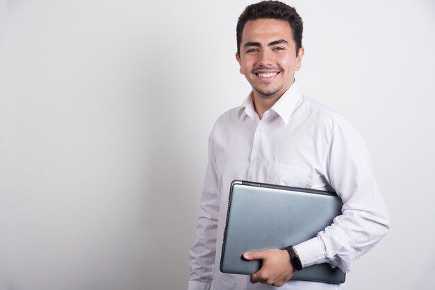 Businessman holding laptop with positive expression on white background.