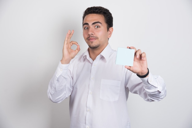 Businessman holding memo pads and showing ok sign on white background.