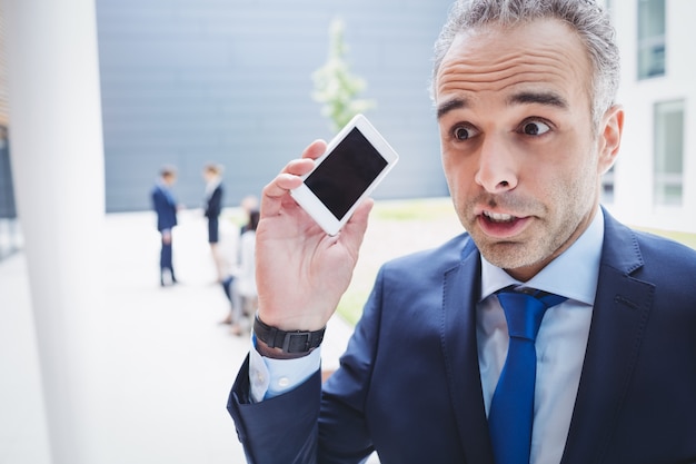 Бизнесмен держит мобильный телефон и хмурится