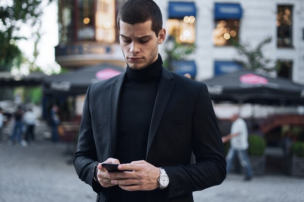 Businessman holding mobile phone and looking at it outdoors