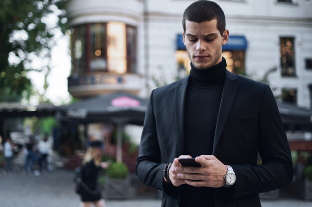 Businessman holding mobile phone and looking at it outdoors