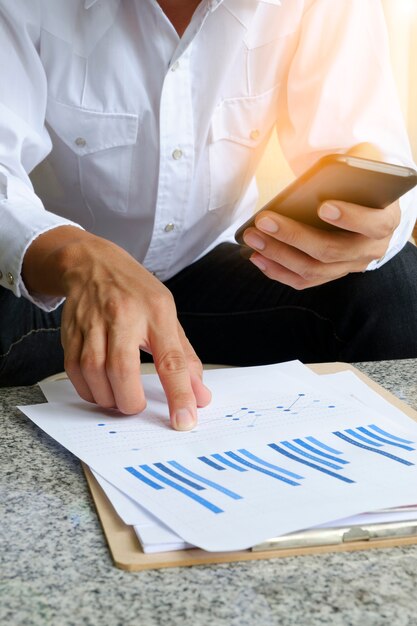 businessman holding mobile phone with analyzing financial chart on tablet , strategy concept , business idea , business concept