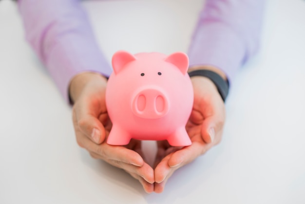 Businessman holding pink piggy bank, isolated on white background.