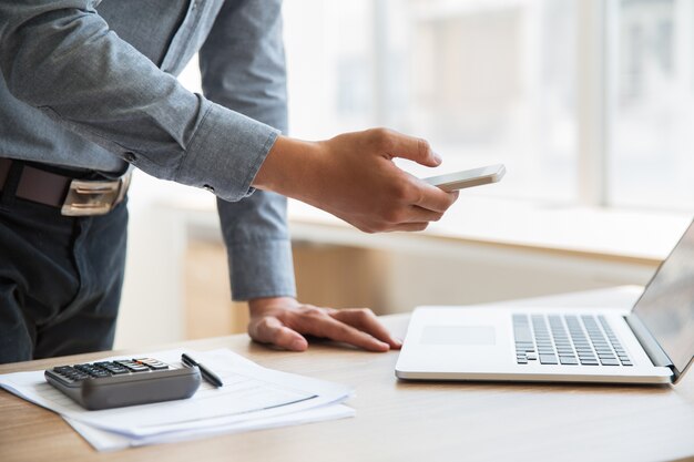 Businessman holding smartphone at laptop in office