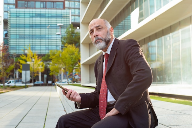 Businessman holding smartphone and looking away