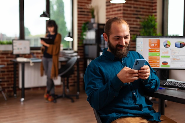 Businessman holding smartphone looking on social media texting with remote friends in startup company office. Manager searching business information developing online communication app.