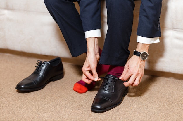 어두운 파란색 양복, 빨간 양말 및 검은 신발 그의 구두 끈을 묶는 시계에서 사업가