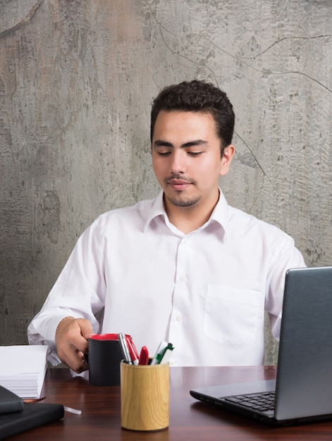 Free photo businessman looking cup of tea at the office desk.