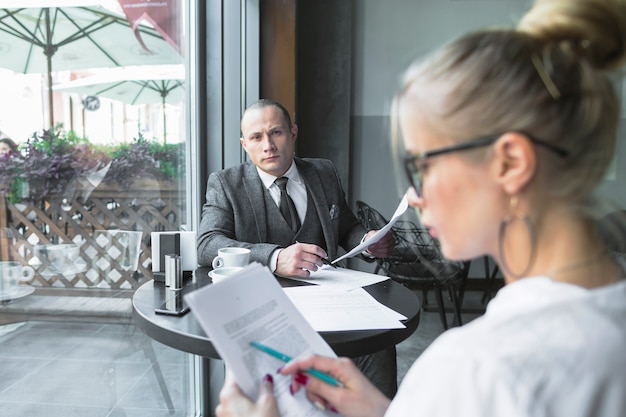 Businessman looking at his colleague examining document in caf�