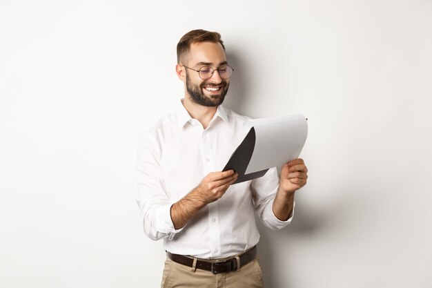 Businessman looking satisfied at documents, reading report and smiling, standing  