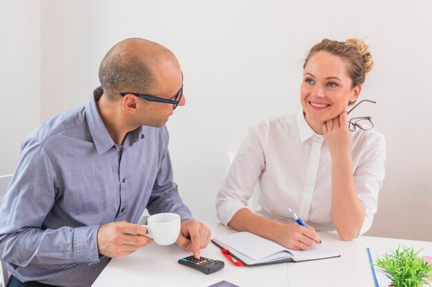 Businessman looking at smiling businesswoman with diary and pen