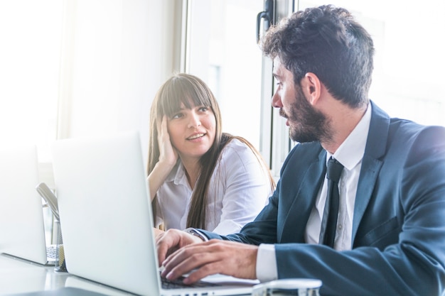 Businessman looking at smiling young woman using laptop