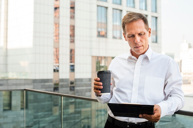 Businessman looking at tablet while holding coffee