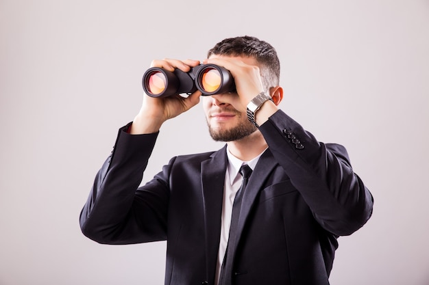 Businessman looking through binoculars isolated on white wall