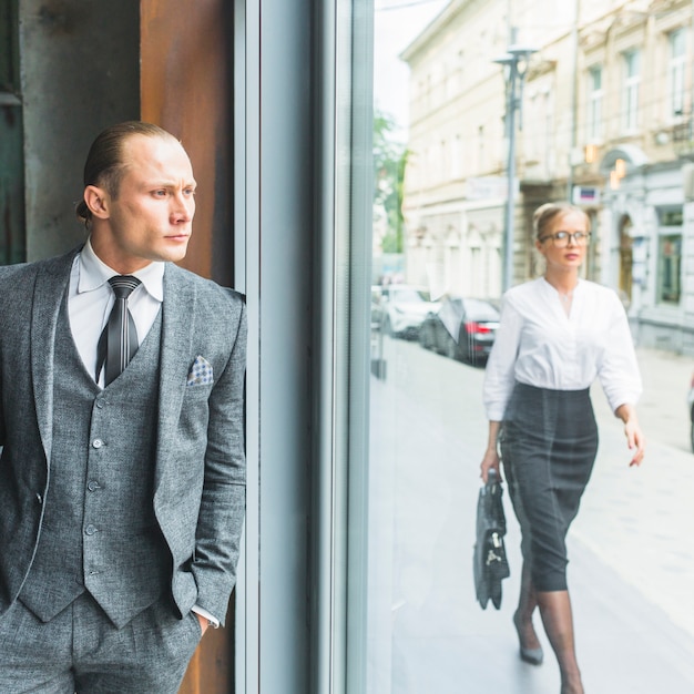 Businessman looking through window while woman walking on sidewalk