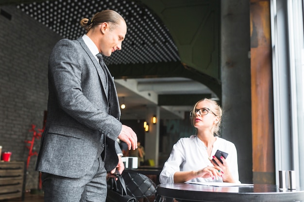 Businessman looking at woman holding mobile phone sitting in caf�