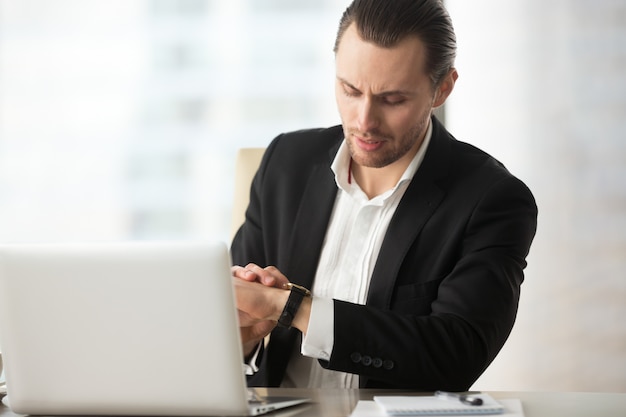 Free photo businessman looking at wristwatch at work desk in office.