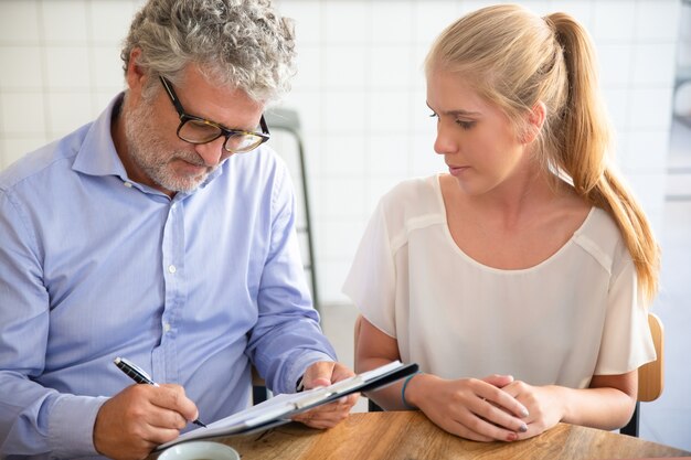 Businessman meeting with agent at co-working, writing in paper, completing and signing agreement form