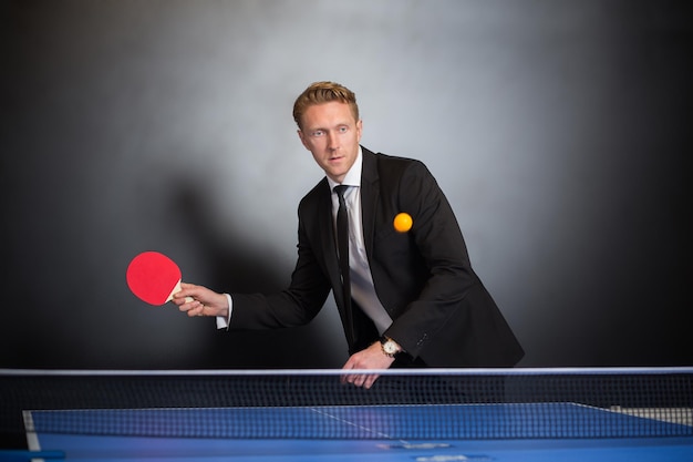 Free photo businessman play tennis with opponent for relax in office across black wall with window.