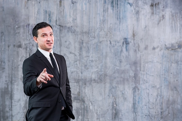 Businessman pointing at camera against grey wall