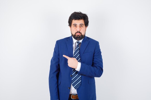 Businessman pointing left with index finger in formal suit and looking serious , front view.